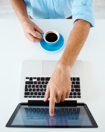 gros-plan-photo-mains-du-jeune-homme-affaires-assis-table-pointant-ecran-ordinateur-portable-tenant-tasse-cafe-interieur-bureau-moderne-blanc
